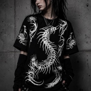 May include: A black short-sleeved t-shirt featuring a large, white, intricate graphic of a skeletal spine-like structure curving down the center, surrounded by detailed illustrations of spider lily flowers with long, thin, flowing petals.