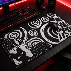 Puede incluir: Alfombrilla de ratón para juegos en blanco y negro con un diseño gráfico que presenta círculos concéntricos, texto y una silueta de gato. Un ratón negro descansa sobre la alfombrilla, colocada sobre un escritorio negro cerca de un teclado.