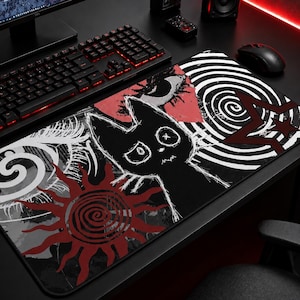 May include: Rectangular black mousepad featuring a cartoon cat design. The illustration includes a black cat with white eyes, a red sun, and a spiral pattern. The mousepad is on a black desk, next to a keyboard and mouse.