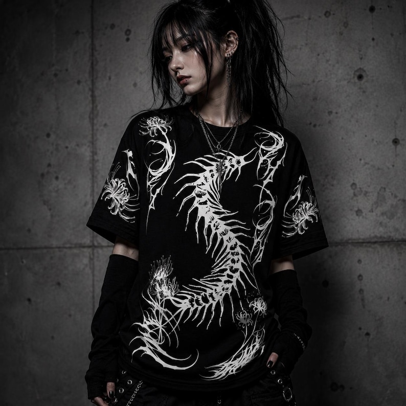May include: A black short-sleeved t-shirt featuring a large, white, intricate graphic of a skeletal spine-like structure curving down the center, surrounded by detailed illustrations of spider lily flowers with long, thin, flowing petals.