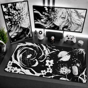 May include: A rectangular desk mat featuring a black and white graphic print of a swirling vortex, spider webs, bats, a moon, and floral elements. The mat is positioned on a desk surface with computer monitors, a game controller, and a mouse.