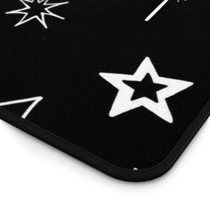 May include: Black surface with white star and geometric designs. The design includes a five-pointed star, a burst, and a triangle. The edge of the surface is black with a thin black border. The design is simple and graphic.
