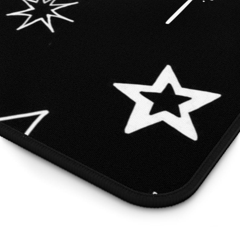 May include: Black surface with white star and geometric designs. The design includes a five-pointed star, a burst, and a triangle. The edge of the surface is black with a thin black border. The design is simple and graphic.