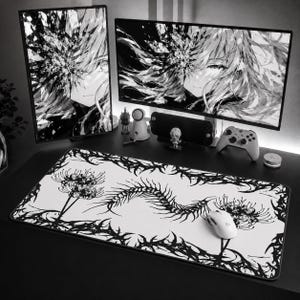 May include: A monochrome gaming setup with two monitors showing anime artwork. A white mouse sits on a large mousepad with a black floral pattern. Other items include a games controller and small figurines.
