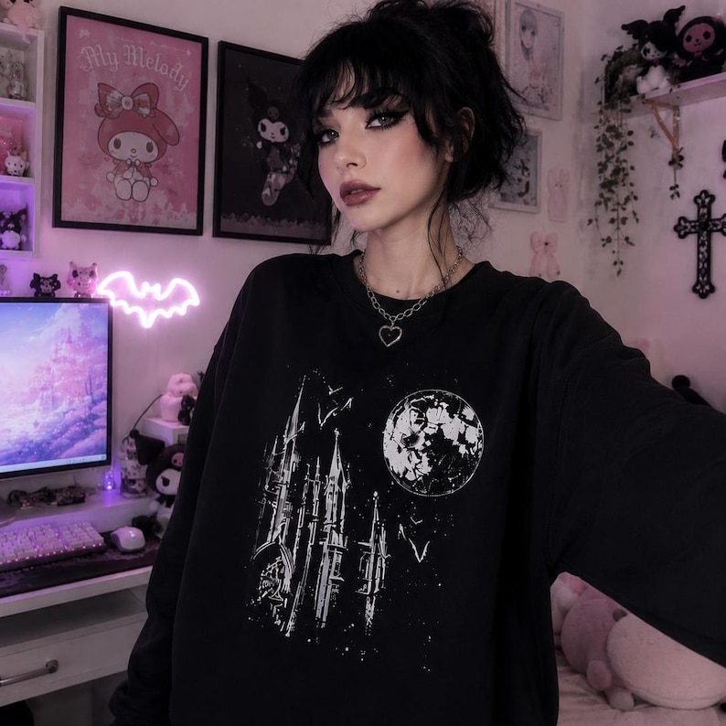 May include: Black sweatshirt featuring a white graphic of a gothic cathedral, a full moon, and flying bats. The design is a distressed, vintage style. The sweatshirt is a crew neck style.