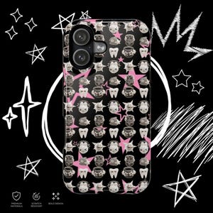 Puede incluir: Funda de teléfono negra con un patrón repetido de dientes, caras y peces de dibujos animados, sobre estrellas rosas. La funda tiene un acabado brillante y presenta un recorte para una cámara de doble lente.