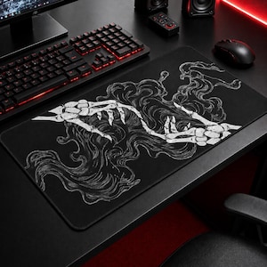 May include: Black rectangular mouse mat with a white skeletal hand design and flowing, smoky details. The mat is on a black desk with a keyboard and mouse visible. The design is gothic or alternative in style.