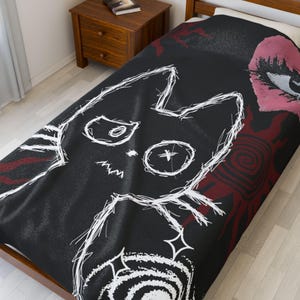 Puede incluir: Funda nórdica negra con un diseño de cara de gato garabateada en blanco. El diseño incluye un ojo rosa y formas abstractas rojas. La ropa de cama está sobre una estructura de cama de madera junto a una mesita de noche de madera.