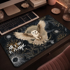 Puede incluir: Alfombrilla de escritorio negra con un diseño de un búho blanco con las alas extendidas sobre un fondo de elementos celestiales. La alfombrilla incluye el texto "all I see is magic" en blanco, con detalles dorados y blancos.