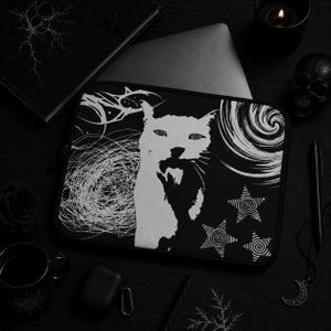 Puede incluir: Una funda para portátil negra con un estampado gráfico blanco de alto contraste de una cara de gato en el centro. El diseño incluye líneas abstractas arremolinadas, un patrón de vórtice circular y tres estrellas con espirales sobre fondo negro.