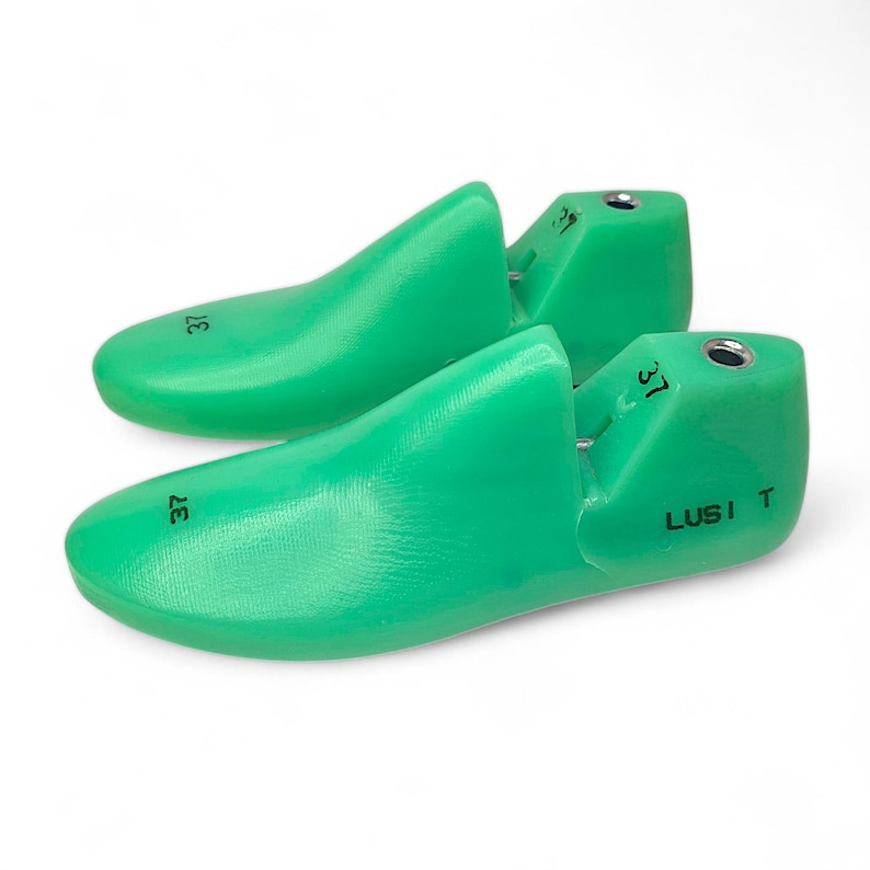 May include: A pair of green plastic shoe trees with the size 37 printed on them. The shoe trees are labeled "LUSI T".