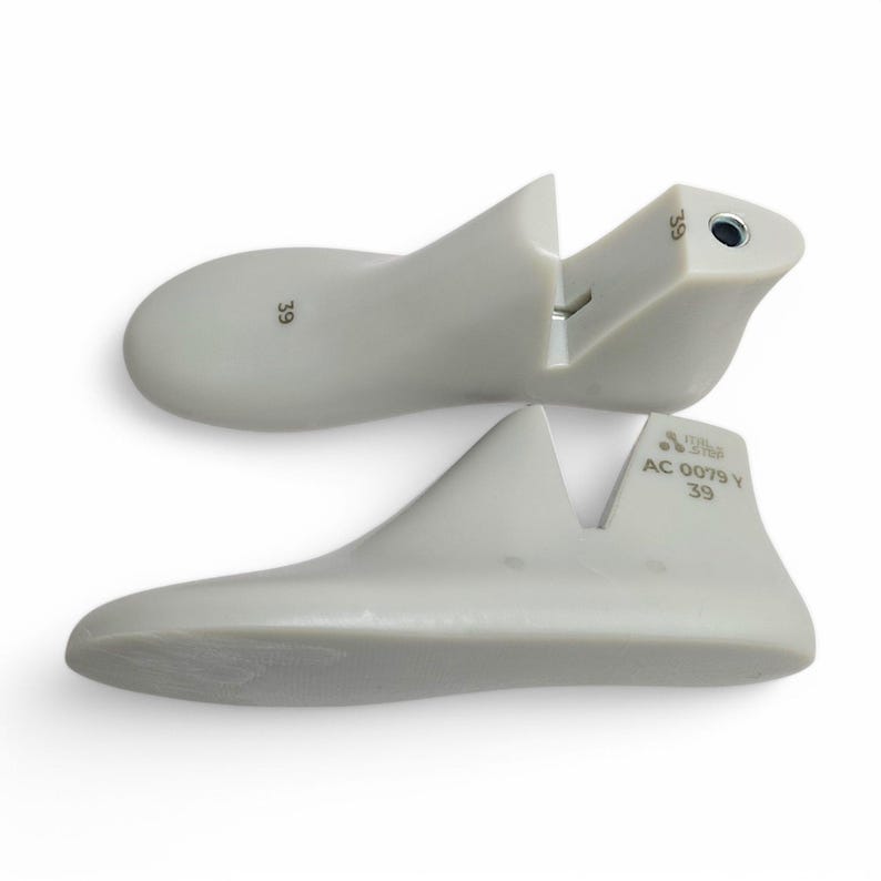 May include: Two light gray shoe lasts, size 39, are displayed against a white background. The lasts are made of a smooth material and are designed to maintain the shape of shoes. One last is split at the heel.