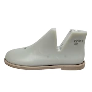 May include: A light gray shoe last with a tan sole. The shoe last has the numbers "39" and "0079 Y" printed on the heel. The shoe last is a mold used in shoemaking to shape shoes.