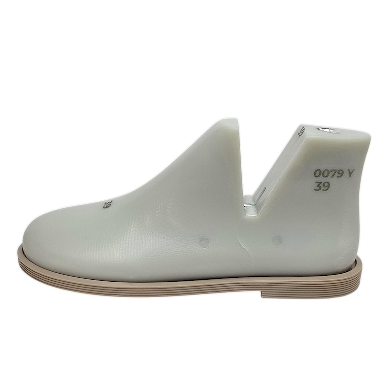 May include: A light gray shoe last with a tan sole. The shoe last has the numbers "39" and "0079 Y" printed on the heel. The shoe last is a mold used in shoemaking to shape shoes.