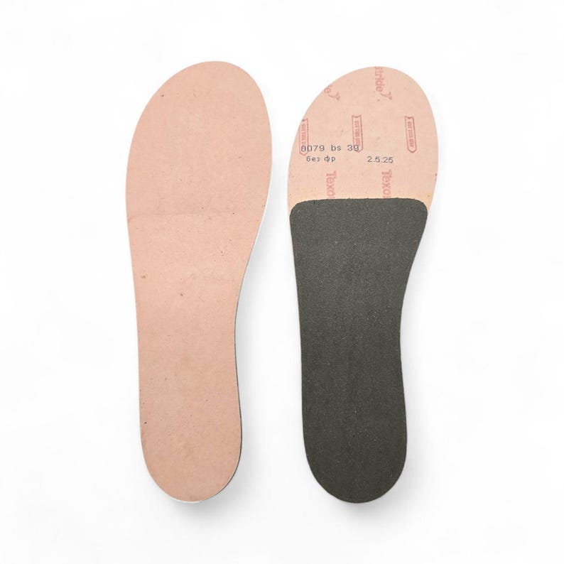 Peut inclure: Deux semelles int&eacute;rieures de chaussures. L'une est de couleur beige clair, l'autre est beige clair avec un talon noir et le texte "Texo". Les semelles sont sur fond blanc.