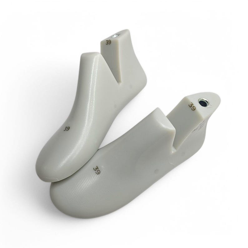 May include: Two light gray shoe lasts, size 39, are displayed against a white background. The shoe forms are made of a smooth, solid material and are designed to maintain the shape of shoes during storage or manufacturing. The number 39 is printed on each form.