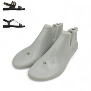 May include: Two white shoe lasts with the number "39" printed on them. The lasts are in the foreground, with two black leather sandals in the background. One sandal has a gold chain detail, and the other has silver studs.