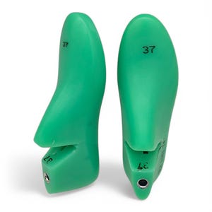 May include: A pair of green plastic shoe trees, each with the number "37" printed on the top. The shoe trees are designed to help maintain the shape of shoes.