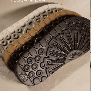 May include: Close-up of three EVA shoe soles in white, tan, and dark gray. The soles have textured patterns and the text "TESSA-4 EVA" is at the top. The soles are stacked at an angle, showcasing their design and material.