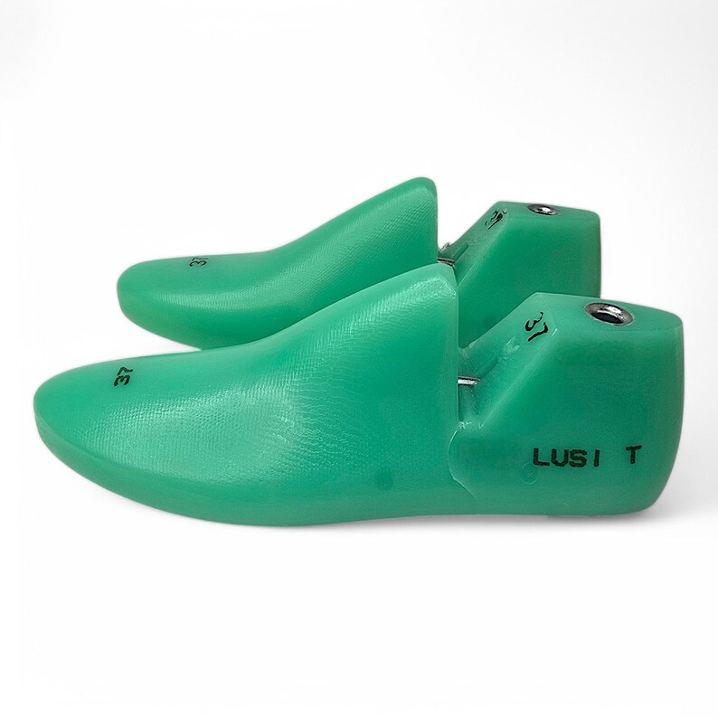 May include: A pair of green plastic shoe trees with the size 37 printed on them. The shoe trees are labeled "LUSI T".