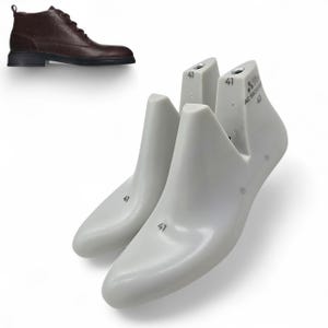 Könnte beinhalten: Ein Paar weiße Schuhleisten mit der Nummer 41, neben einem braunen Lederstiefel. Die Schuhleisten bestehen aus einem glatten, festen Material und dienen dazu, die Form der Schuhe zu erhalten.