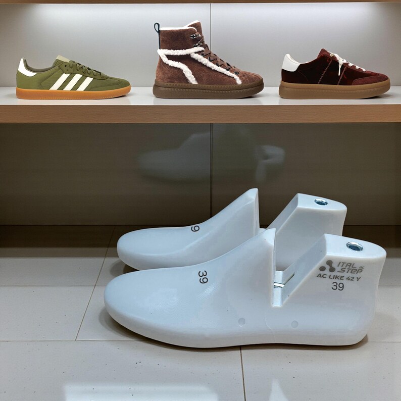 May include: A display of footwear, including green sneakers with white stripes, brown high-top boots with white trim, and burgundy sneakers. Two white shoe lasts with the number 39 are in the foreground.