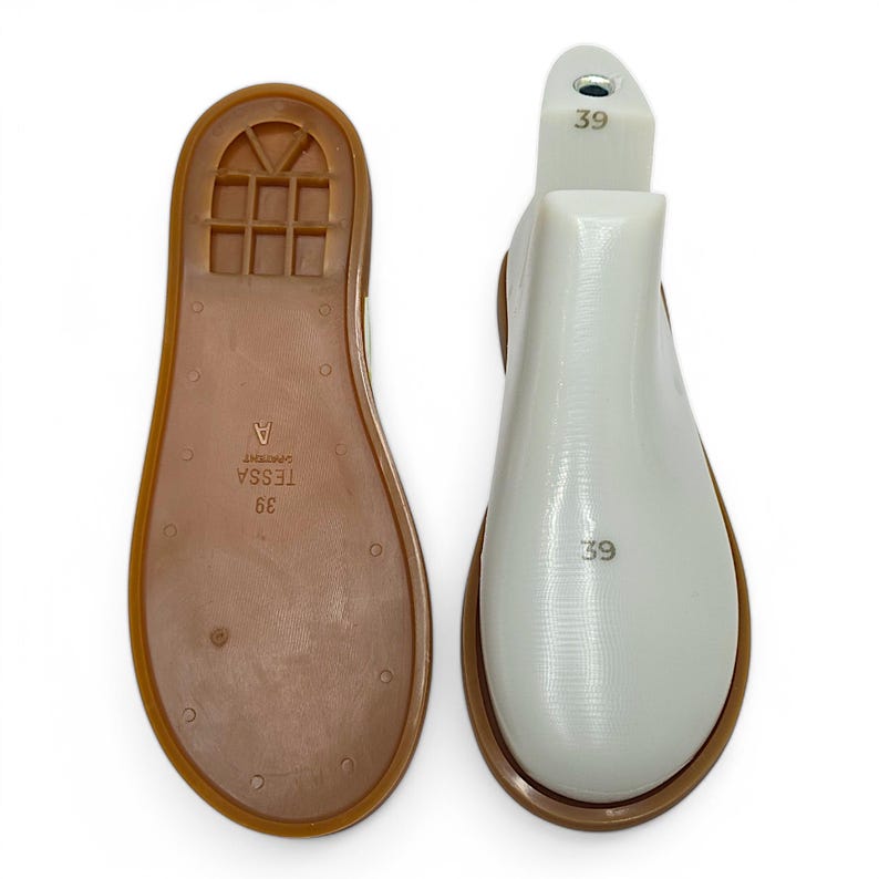 May include: Two shoe lasts, one brown and one white, are displayed against a white background. The brown sole is marked with "39 TESSA A" and has a textured pattern. The white last is marked with "39".