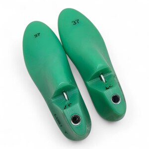 May include: Two green plastic shoe trees, each with a size 37 printed on them. The shoe trees are designed to help maintain the shape of shoes.