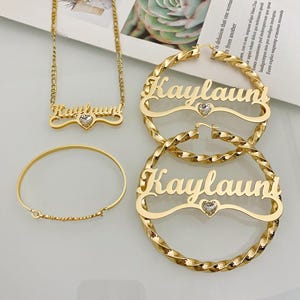 May include: Gold-tone necklace, bracelet, and hoop earrings with the name "Kaylauni" and a small heart-shaped rhinestone charm.