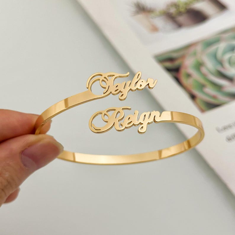 May include: Gold-toned bangle bracelet with two names, "Taylor" and "Reign", written in a cursive script.
