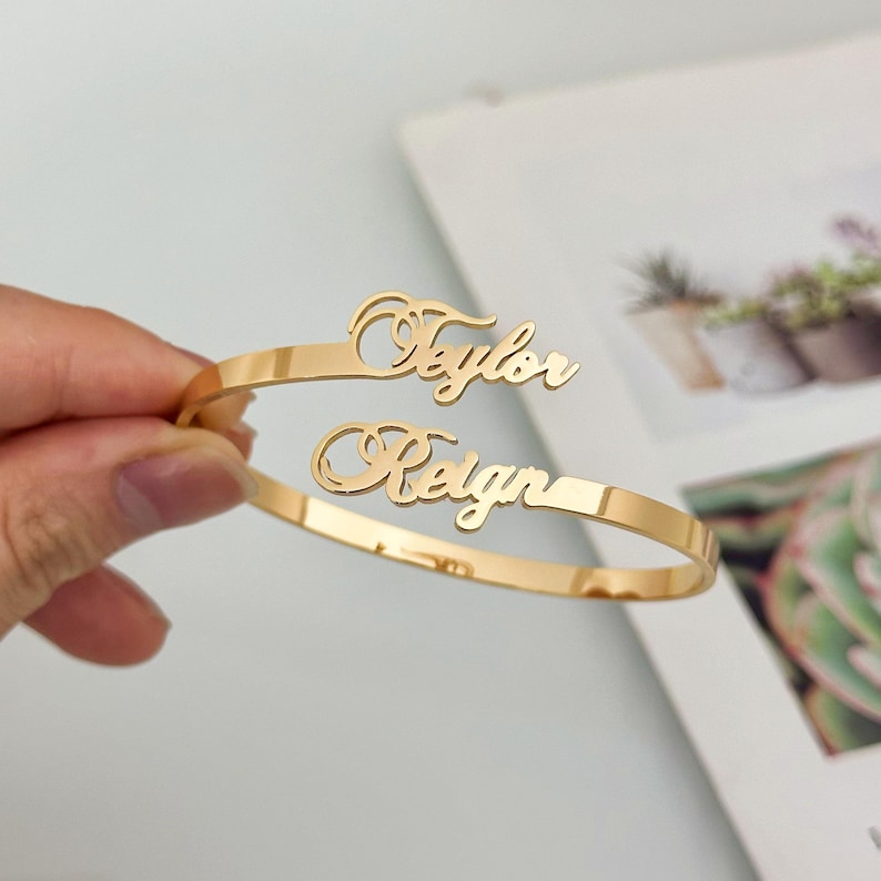 May include: Gold-toned bangle bracelet with the names "Taylor" and "Reign" engraved in a cursive font.