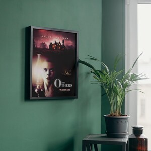 May include: A movie poster for the film "The Others" starring Nicole Kidman. The poster features a woman holding a lantern in a dark, shadowy room. The text "The Others" is in large, bold letters at the bottom of the poster.