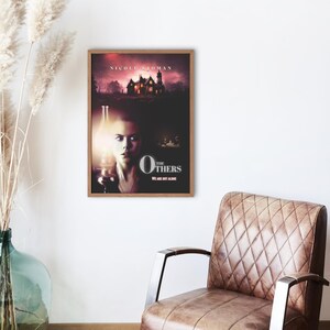 May include: Movie poster for the film "The Others" starring Nicole Kidman. The poster features a woman holding a lantern in front of a dark, ominous house. The text "The Others" is in large, white letters with the tagline "We are not alone."