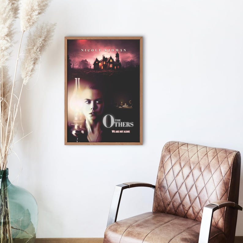 May include: Movie poster for the film "The Others" starring Nicole Kidman. The poster features a woman holding a lantern in front of a dark, ominous house. The text "The Others" is in large, white letters with the tagline "We are not alone."