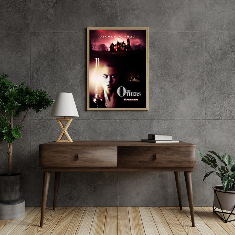 May include: A movie poster for the film "The Others" starring Nicole Kidman. The poster features a woman with a pale complexion and dark hair standing in front of a large, dark house. The text "The Others" is written in white letters on a black background.