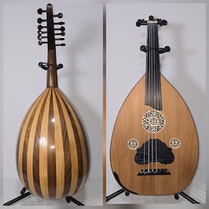 Puede incluir: Se muestran dos ouds, un tipo de laúd. Uno tiene un patrón a rayas de madera clara y oscura. El otro tiene un cuerpo de madera clara con tallas decorativas y una boca oscura. Ambos están sobre soportes negros.