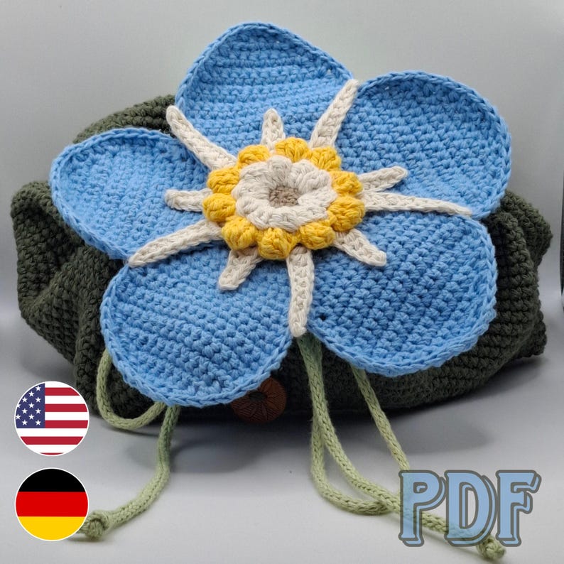 May include: A handmade crochet bag featuring a large blue flower with a yellow and cream center. The flower is attached to a green base, with green drawstring cords. The bag is a unique, handcrafted item.