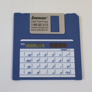 May include: A blue floppy disk shaped calculator with a silver metal sliding shutter. The label reads inmac, Call Toll-Free 1-800-387-2173, Toronto (416) 826-1515, Faxline (416) 826-4734. The digital display shows 455 and the keypad has white buttons.