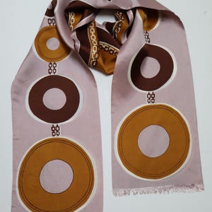 May include: A vintage silk scarf in shades of mauve, brown, and gold. The scarf features a repeating pattern of large circles with a chain-like design in the centre. The ends have a fringed edge.