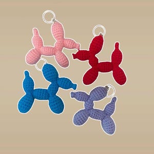 May include: Four crocheted balloon dog keychains in pink, red, blue, and purple.