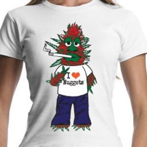 Puede incluir: Una camiseta blanca con un personaje de dibujos animados que lleva pantalones vaqueros azules y una camiseta roja que dice "Me encantan las Nuggets". El personaje es verde con el pelo rojo y fuma un cigarrillo.