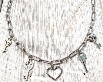 Può includere: Collana color argento con ciondoli a forma di chiave e cuore. La collana ha un design a catena con vari ciondoli a forma di chiave e un ciondolo a forma di cuore. Le chiavi hanno design diversi, aggiungendo un tocco unico ai gioielli.