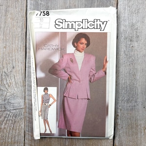Può includere: Cartamodello Simplicity con un tailleur rosa. Il modello include una foto del completo e il nome "Cathy Hardwick". Il numero del modello è 7758, taglia 10. La busta è su una superficie di legno.