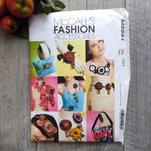 以下が含まれることがあります： 花柄のアクセサリーがデザインされた、マッコールズ ファッション アクセサリーの縫製パターンブックレット。ネックレス、ブレスレット、バッグ、ヘッドバンドなど、さまざまなカラフルな布製のアクセサリーが掲載されています。パターン番号はM5901です。