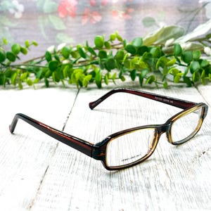 May include: Brown and tortoise shell eyeglasses with rectangular frames. The glasses have a dark brown frame and temples, with a lighter brown and tortoise shell pattern on the front. The lenses have the text "DEMO LENS ONLY".