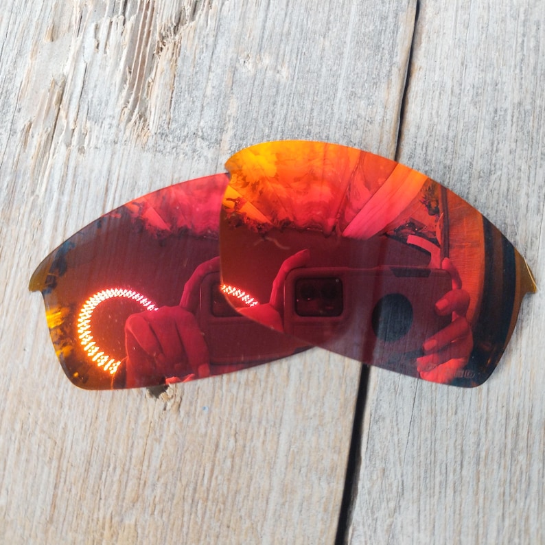 Puede incluir: Un par de lentes de repuesto para gafas de sol, de color rojo y naranja espejado. Las lentes son curvadas y tienen una superficie reflectante.