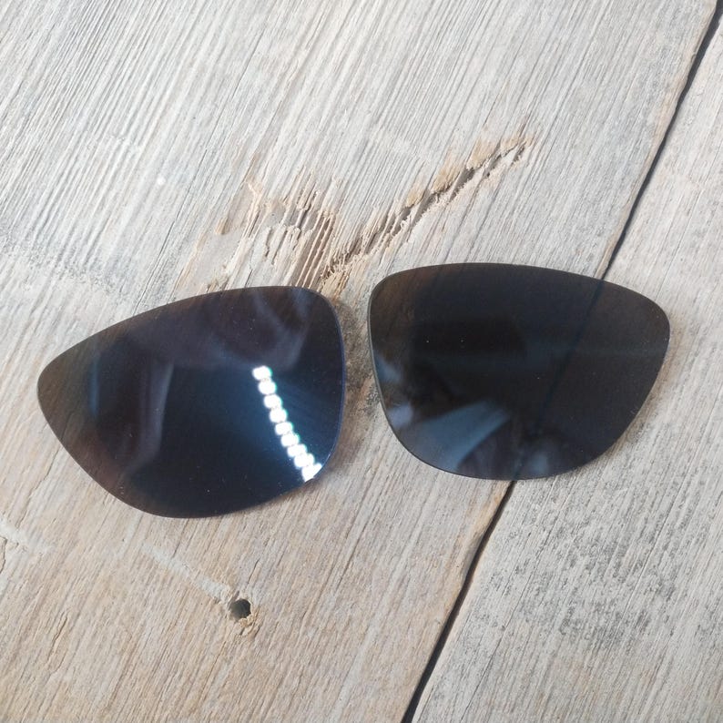 May include: Two dark brown replacement lenses for sunglasses. The lenses are oval shaped and have a slight curve.
