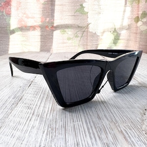 Puede incluir: Gafas de sol negras con un dise&ntilde;o geom&eacute;trico &uacute;nico. Las monturas son brillantes y angulares, con una forma afilada y puntiaguda. Las lentes son oscuras y las gafas de sol tienen una est&eacute;tica moderna y atrevida. El texto "CHINA NFASH1" est&aacute; impreso en la montura.