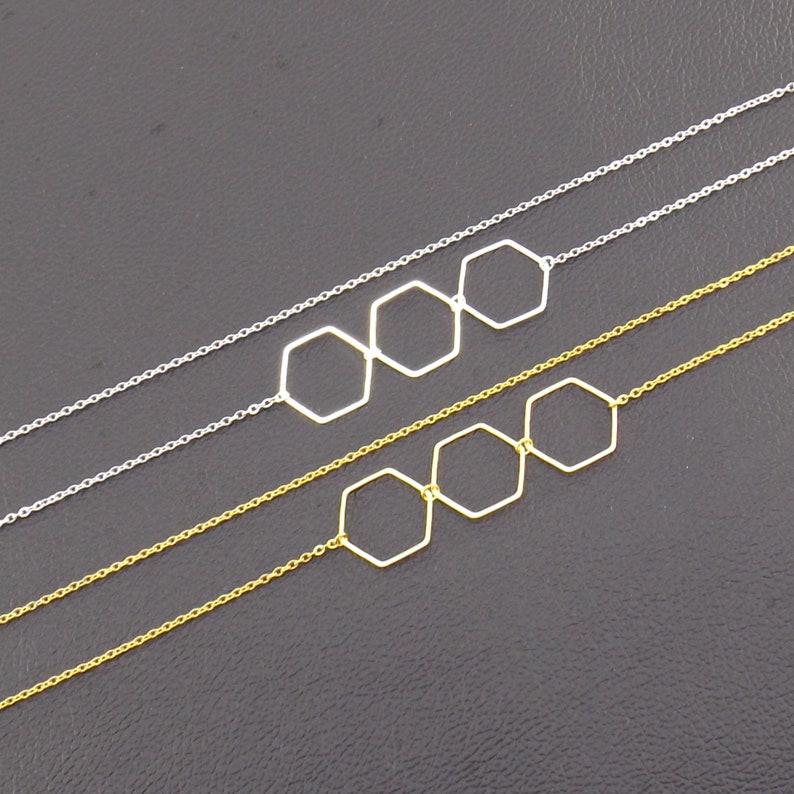 Op de afbeelding: Twee kettingen met drie zeshoekige hangerbedels. De bovenste ketting is zilver en de onderste ketting is goud.