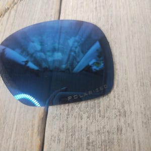 May include: A close-up of a blue polarised lens for sunglasses. The lens has a slight curve and the word "POLARIZED" is printed on the bottom.